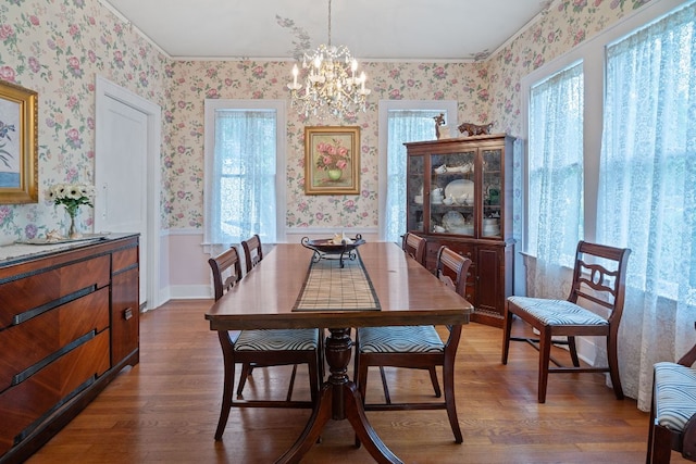 dining space with wallpapered walls, a chandelier, dark wood-style floors, and ornamental molding