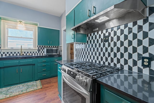 kitchen featuring a sink, appliances with stainless steel finishes, dark countertops, and ventilation hood