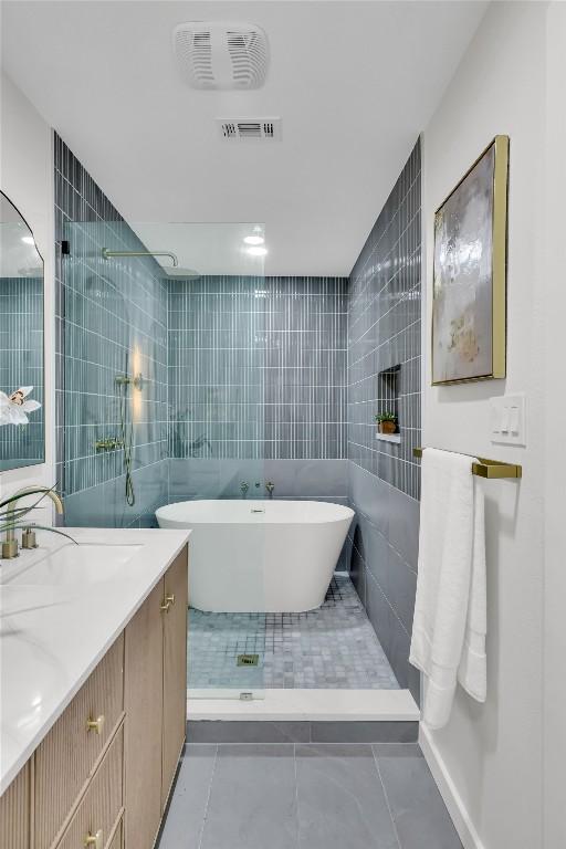 bathroom featuring visible vents, tile walls, a tile shower, vanity, and a soaking tub