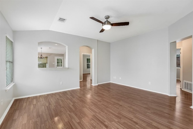 empty room featuring arched walkways, ceiling fan with notable chandelier, wood finished floors, and visible vents