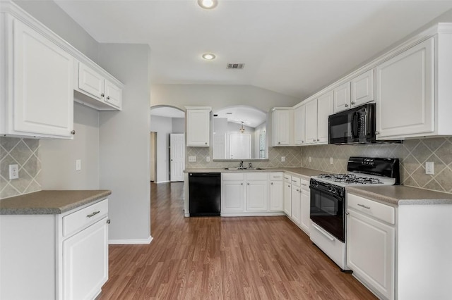kitchen featuring visible vents, decorative backsplash, arched walkways, black appliances, and vaulted ceiling