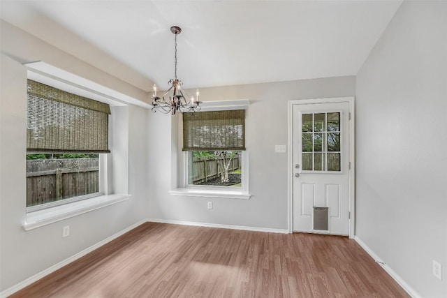 unfurnished dining area featuring an inviting chandelier, baseboards, and wood finished floors