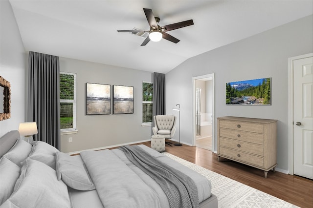 bedroom with baseboards, vaulted ceiling, ensuite bath, and dark wood-type flooring