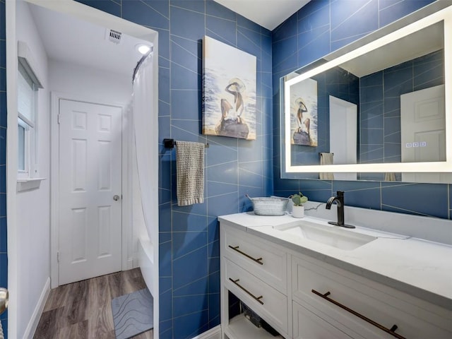 full bath with wood finished floors, tile walls, vanity, and shower / bathtub combination with curtain