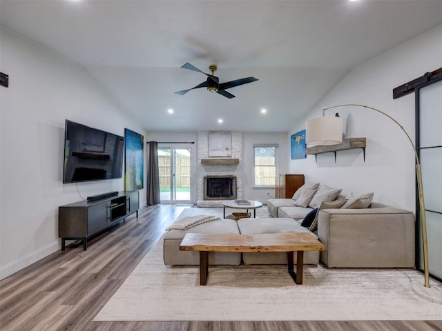 living room with lofted ceiling, a ceiling fan, wood finished floors, baseboards, and a stone fireplace