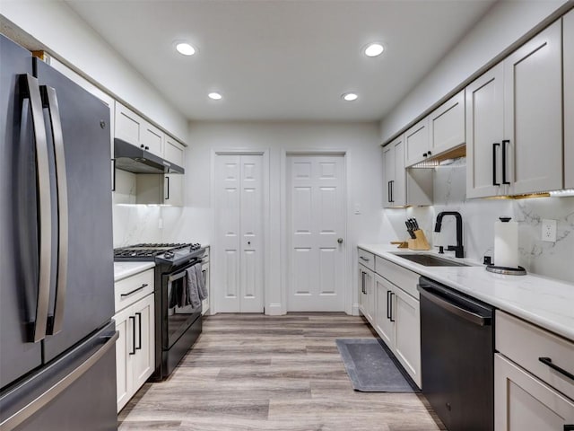 kitchen with black gas stove, freestanding refrigerator, dishwashing machine, a sink, and under cabinet range hood