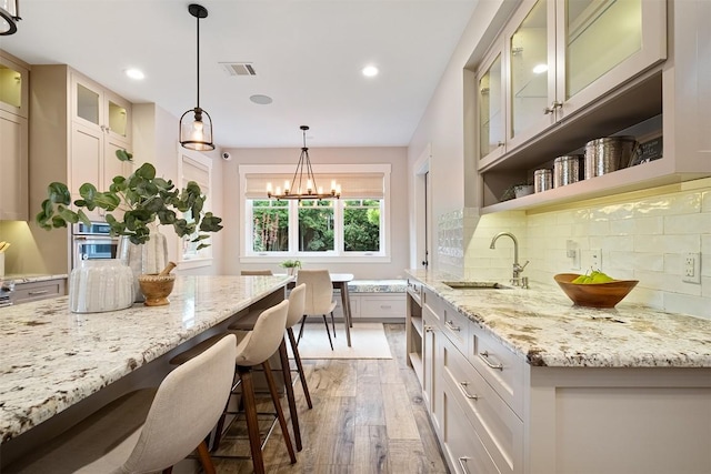 5517 Woodview Ave, Austin, TX 78756 - kitchen featuring visible vents, light stone countertops, a sink, light wood finished floors, and a breakfast bar