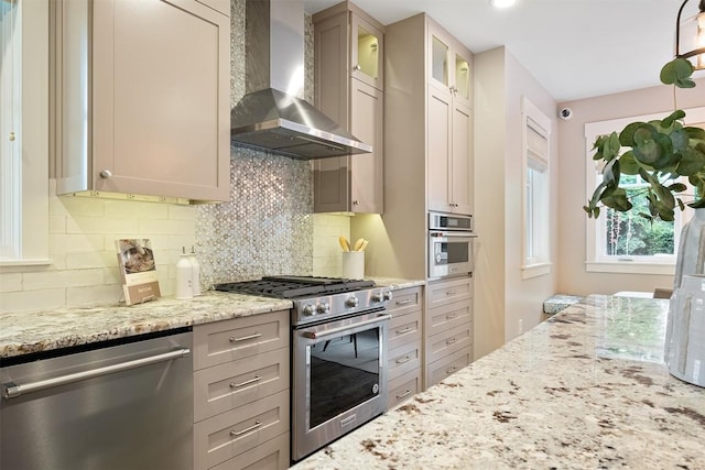 5517 Woodview Ave, Austin, TX 78756 - kitchen featuring wall chimney range hood, appliances with stainless steel finishes, tasteful backsplash, light stone countertops, and glass insert cabinets
