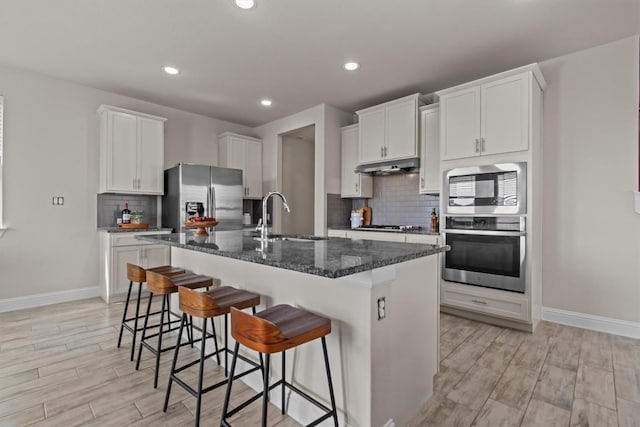 kitchen with decorative backsplash, a kitchen breakfast bar, a kitchen island with sink, a sink, and stainless steel appliances