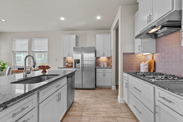 kitchen with appliances with stainless steel finishes, a sink, dark stone countertops, white cabinetry, and under cabinet range hood