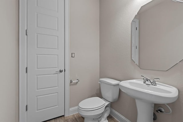 bathroom featuring baseboards, wood finished floors, and toilet