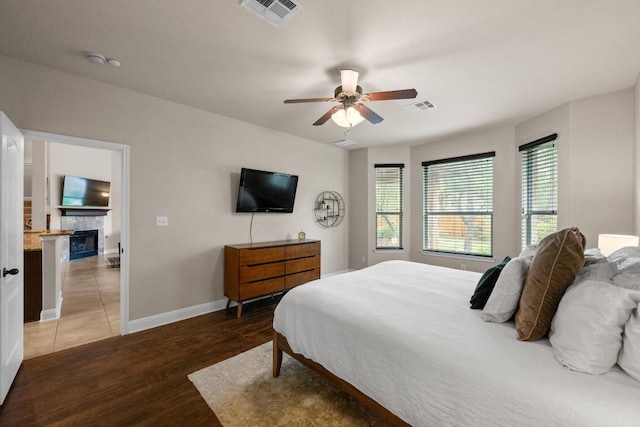 bedroom featuring baseboards, a fireplace, wood finished floors, and visible vents