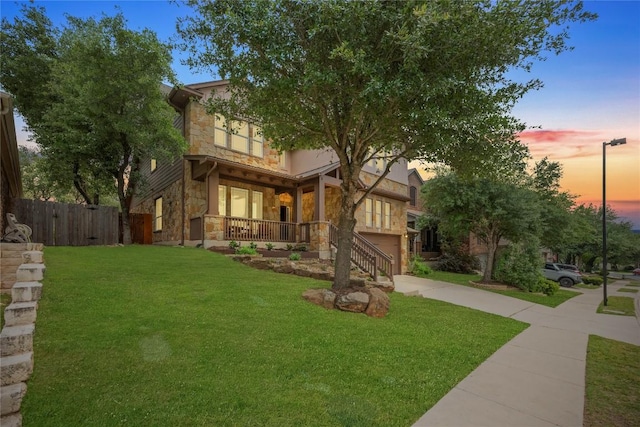 view of front of house with a lawn, fence, covered porch, stone siding, and an attached garage