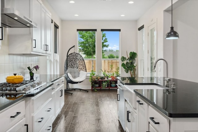kitchen with wall chimney range hood, dark countertops, appliances with stainless steel finishes, white cabinetry, and dark wood-type flooring