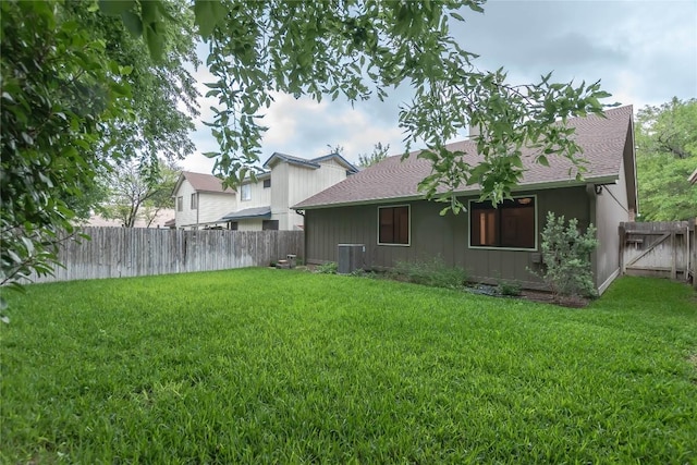 back of property with a yard, fence, central AC unit, and roof with shingles