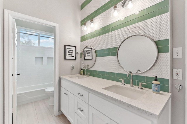 full bath featuring double vanity, a sink, decorative backsplash, and toilet