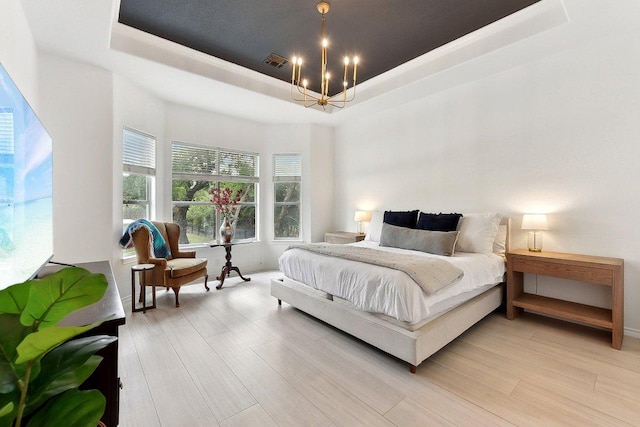 bedroom featuring an inviting chandelier, a raised ceiling, light wood finished floors, and visible vents