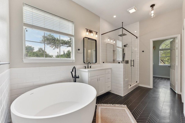 bathroom with tile walls, a freestanding bath, a shower stall, and vanity