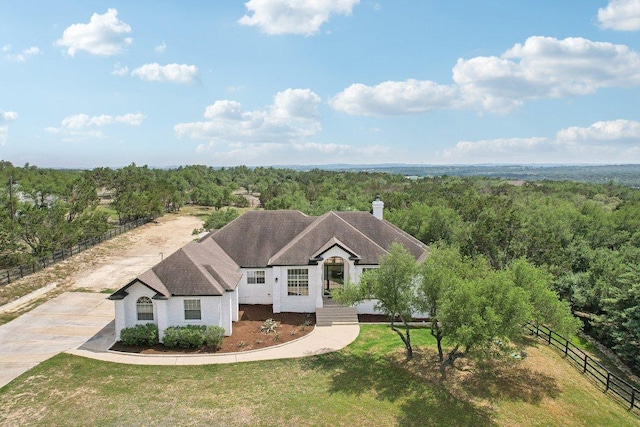 view of front facade with a forest view, fence, a chimney, and a front yard