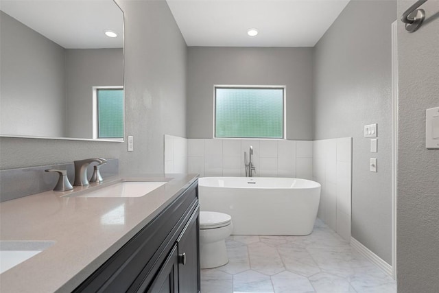 bathroom with double vanity, a sink, toilet, a textured wall, and a soaking tub