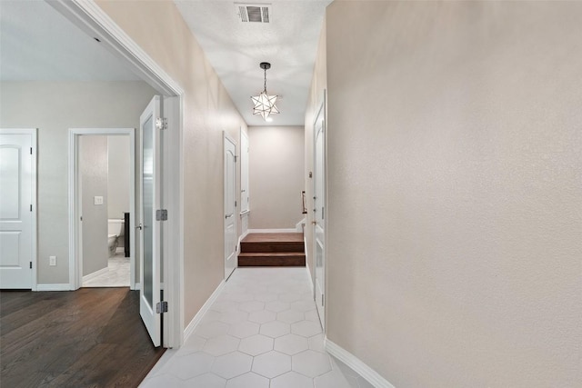 hall with visible vents, baseboards, wood finished floors, and an inviting chandelier