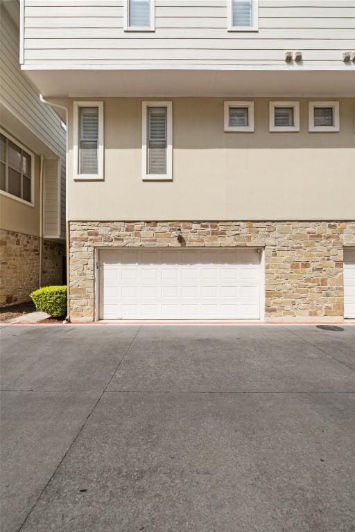 exterior space featuring concrete driveway, stucco siding, stone siding, and a garage