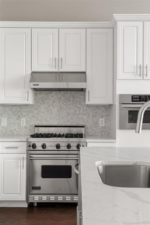 kitchen with white cabinets, appliances with stainless steel finishes, a sink, backsplash, and under cabinet range hood