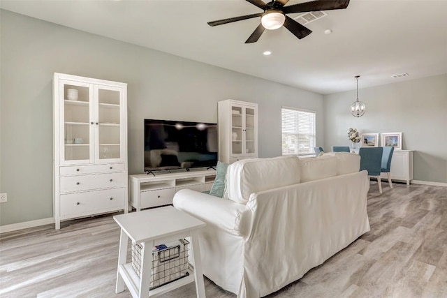 living room with baseboards, ceiling fan with notable chandelier, light wood-style flooring, and visible vents