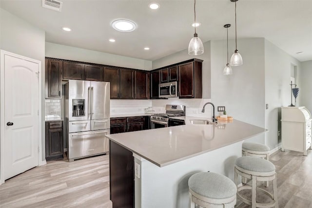 kitchen featuring visible vents, a sink, light wood finished floors, a peninsula, and stainless steel appliances