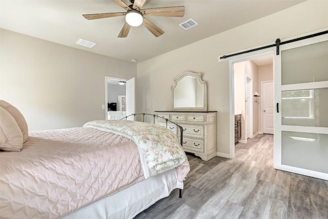 bedroom featuring visible vents, a barn door, baseboards, and light wood-type flooring