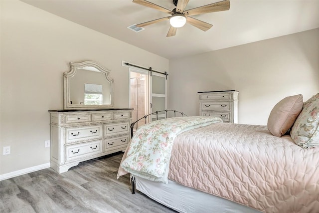 bedroom featuring a barn door, a ceiling fan, baseboards, wood finished floors, and visible vents