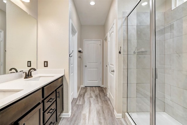 bathroom with double vanity, wood finished floors, baseboards, a sink, and a stall shower