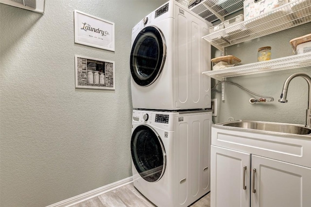 washroom with stacked washer / dryer, cabinet space, a sink, light wood-style floors, and a textured wall