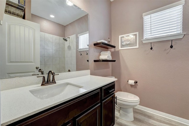 full bath with vanity, wood finished floors, toilet, baseboards, and a tile shower