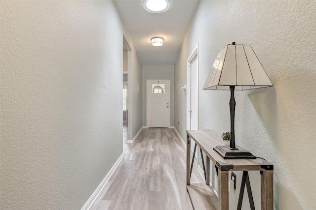 doorway with a textured wall, baseboards, and light wood finished floors