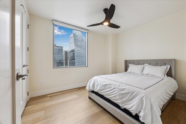 bedroom featuring baseboards, ceiling fan, light wood-style flooring, and a view of city