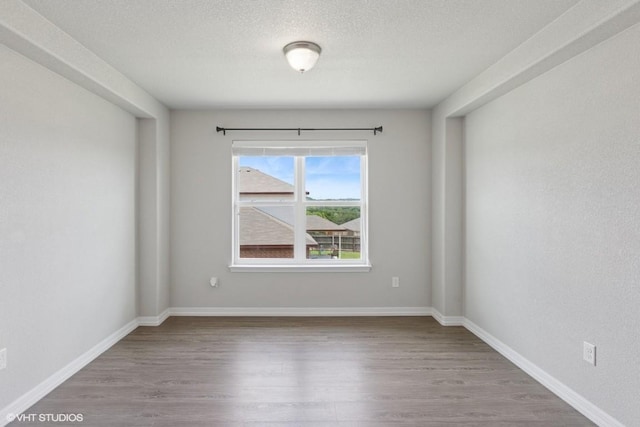 unfurnished room featuring baseboards, a textured ceiling, and wood finished floors