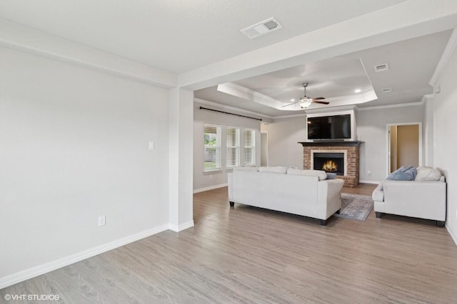 living area with a brick fireplace, a ceiling fan, baseboards, a tray ceiling, and visible vents