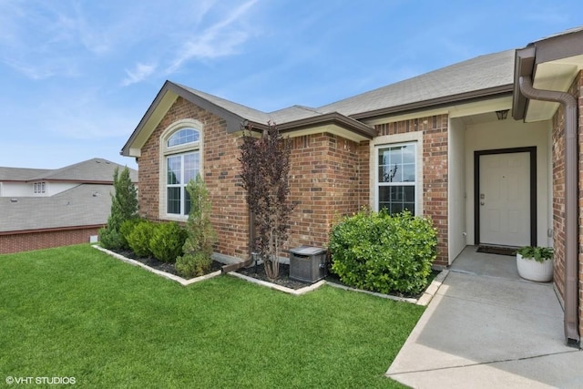entrance to property with a lawn, brick siding, and a shingled roof