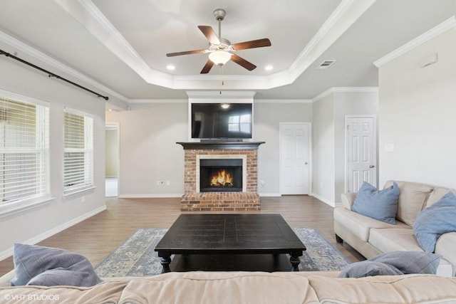 living area with ceiling fan, a tray ceiling, wood finished floors, and a brick fireplace
