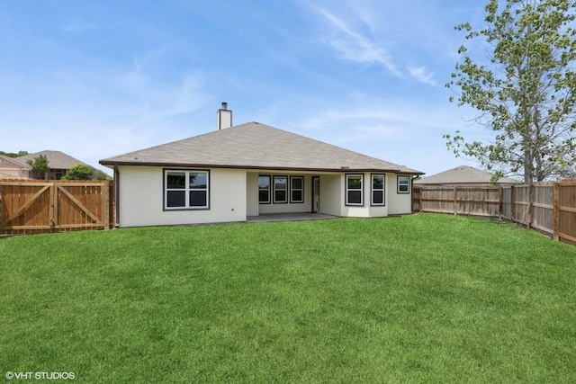 rear view of house with a chimney, a fenced backyard, a yard, a patio, and stucco siding