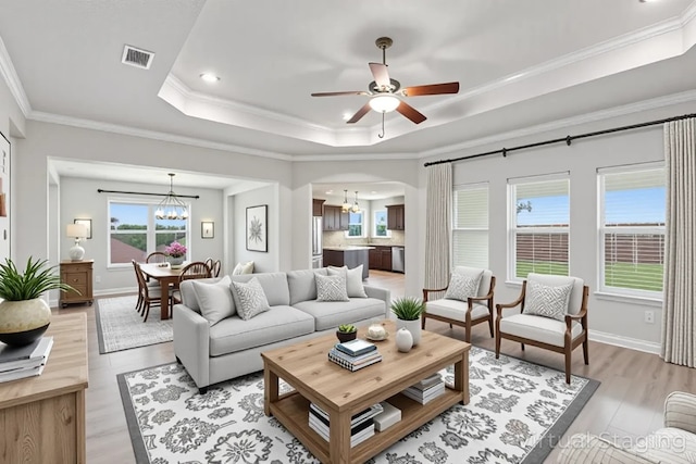 2403 Spirit Dancer Dr, Copperas Cove, TX 76522 - living room featuring a tray ceiling, a chandelier, light wood-type flooring, a ceiling fan, and arched walkways