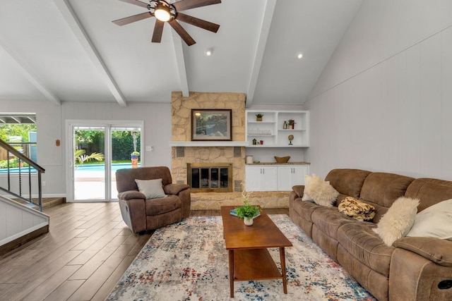 living room with ceiling fan, a stone fireplace, wood finished floors, stairway, and vaulted ceiling with beams