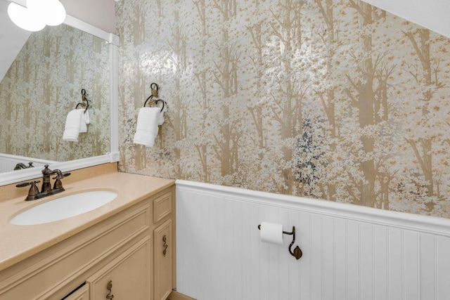 bathroom featuring a wainscoted wall, vanity, and wallpapered walls