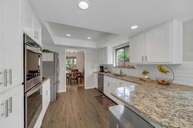 kitchen with a sink, appliances with stainless steel finishes, white cabinets, and a raised ceiling