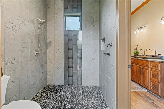 bathroom featuring vanity, wood finished floors, a tile shower, and toilet