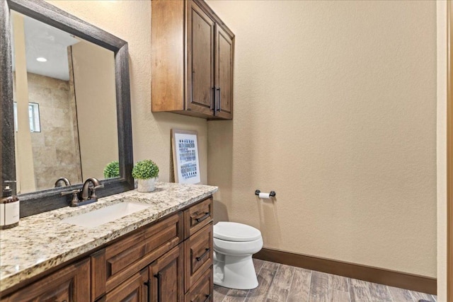 bathroom featuring wood finished floors, vanity, baseboards, toilet, and a textured wall