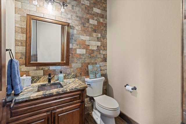 half bathroom with vanity, baseboards, and toilet
