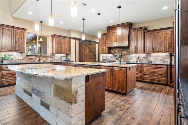kitchen featuring visible vents, an island with sink, backsplash, and dark wood-style floors