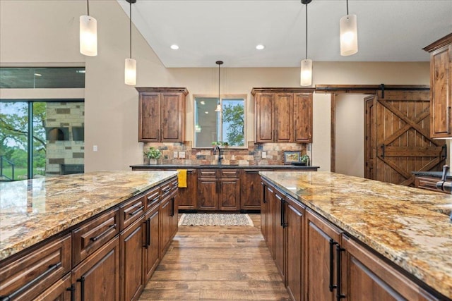 kitchen with backsplash, pendant lighting, light stone countertops, a sink, and light wood-style floors